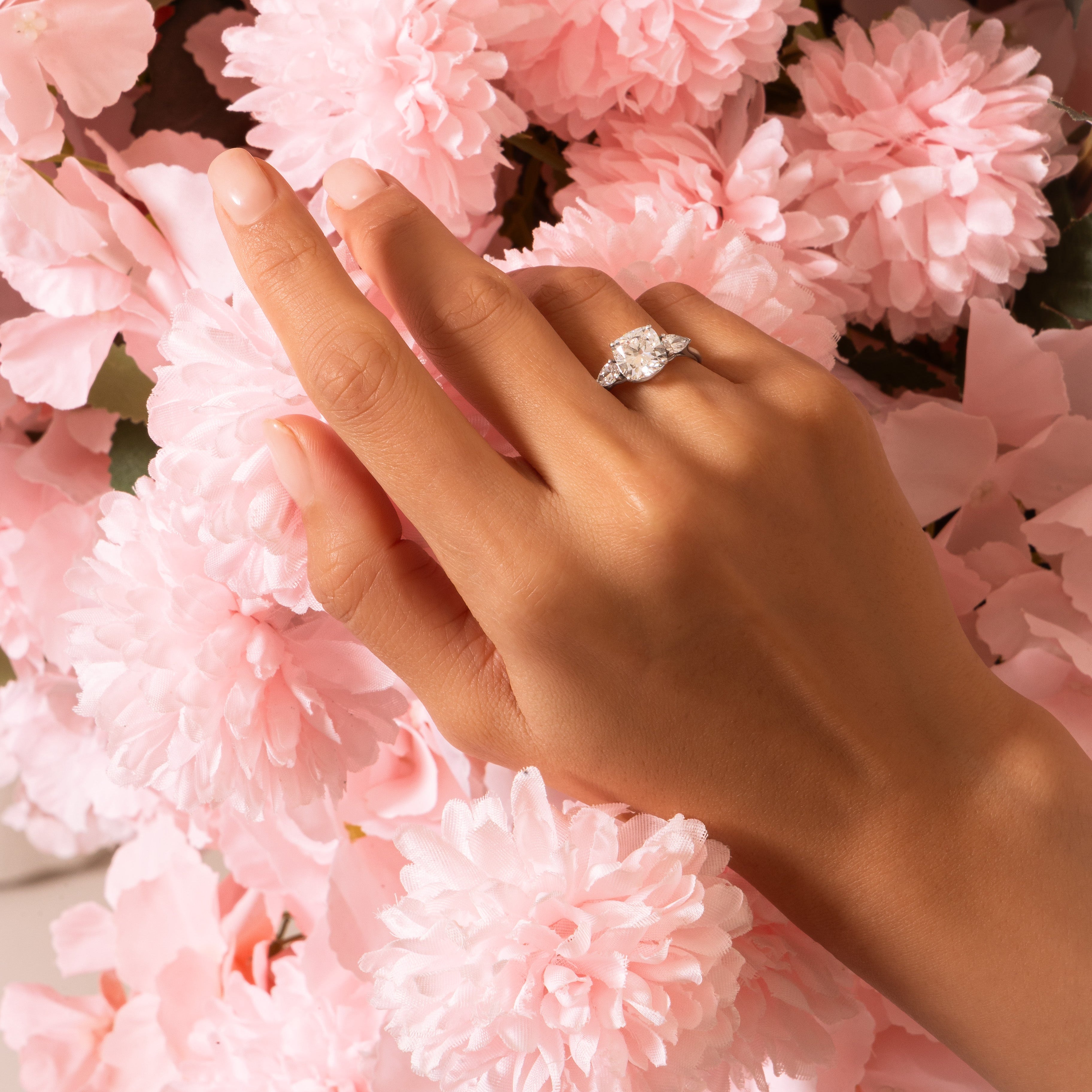 Hand wearing a diamond ring with pink flowers in the background