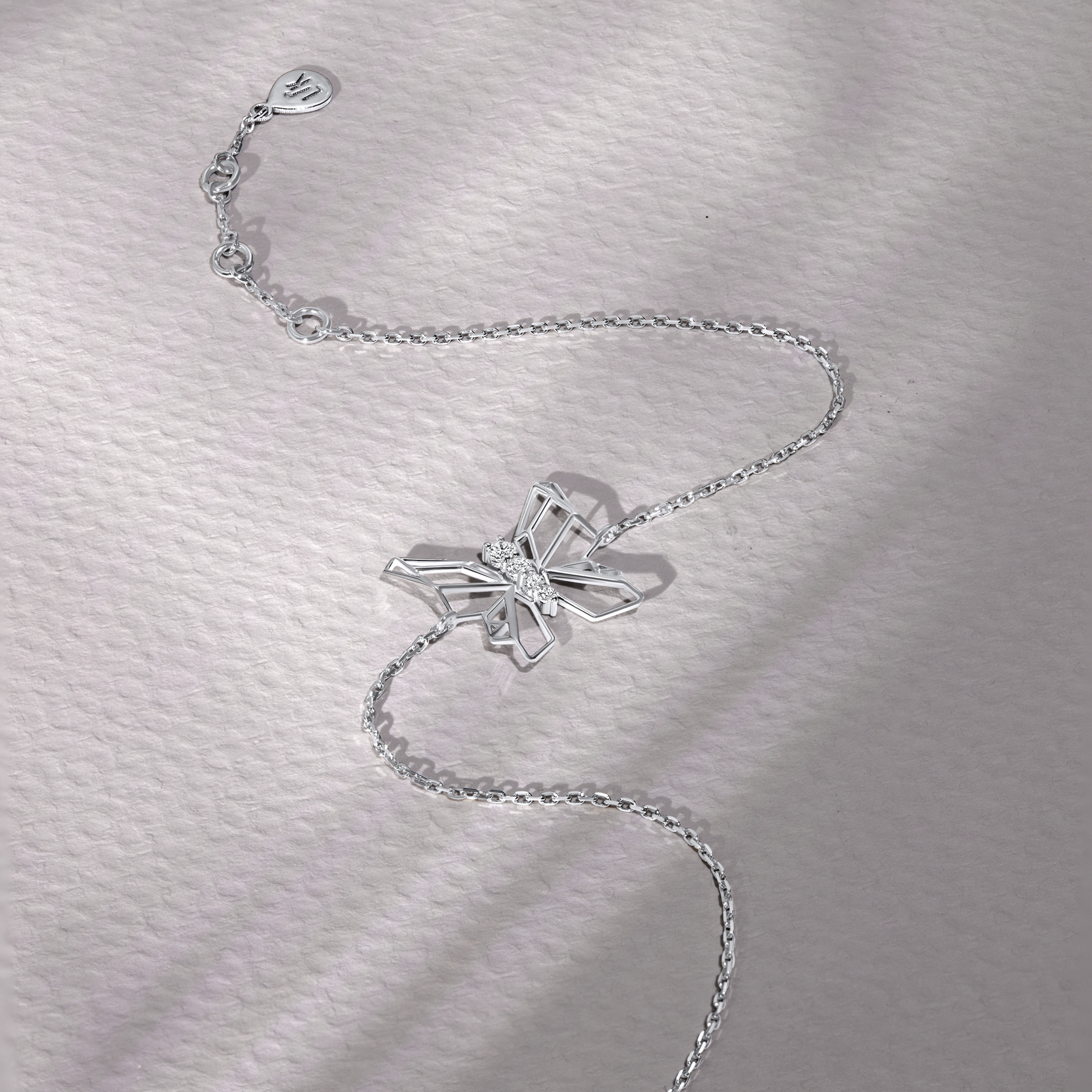 white gold bracelet with a butterfly charm on a textured gray background
