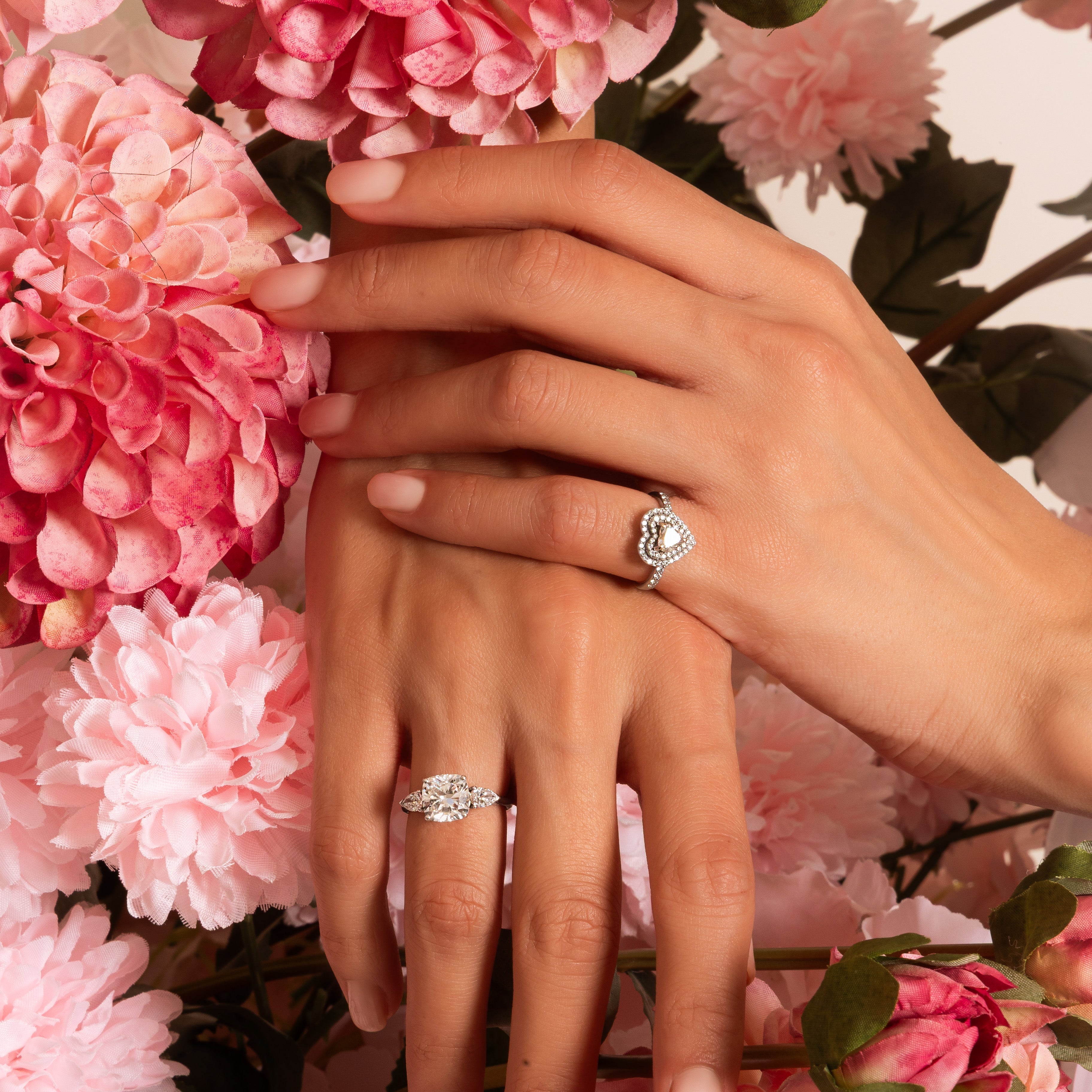 Close-up of hands wearing diamond rings with pink flowers in the background