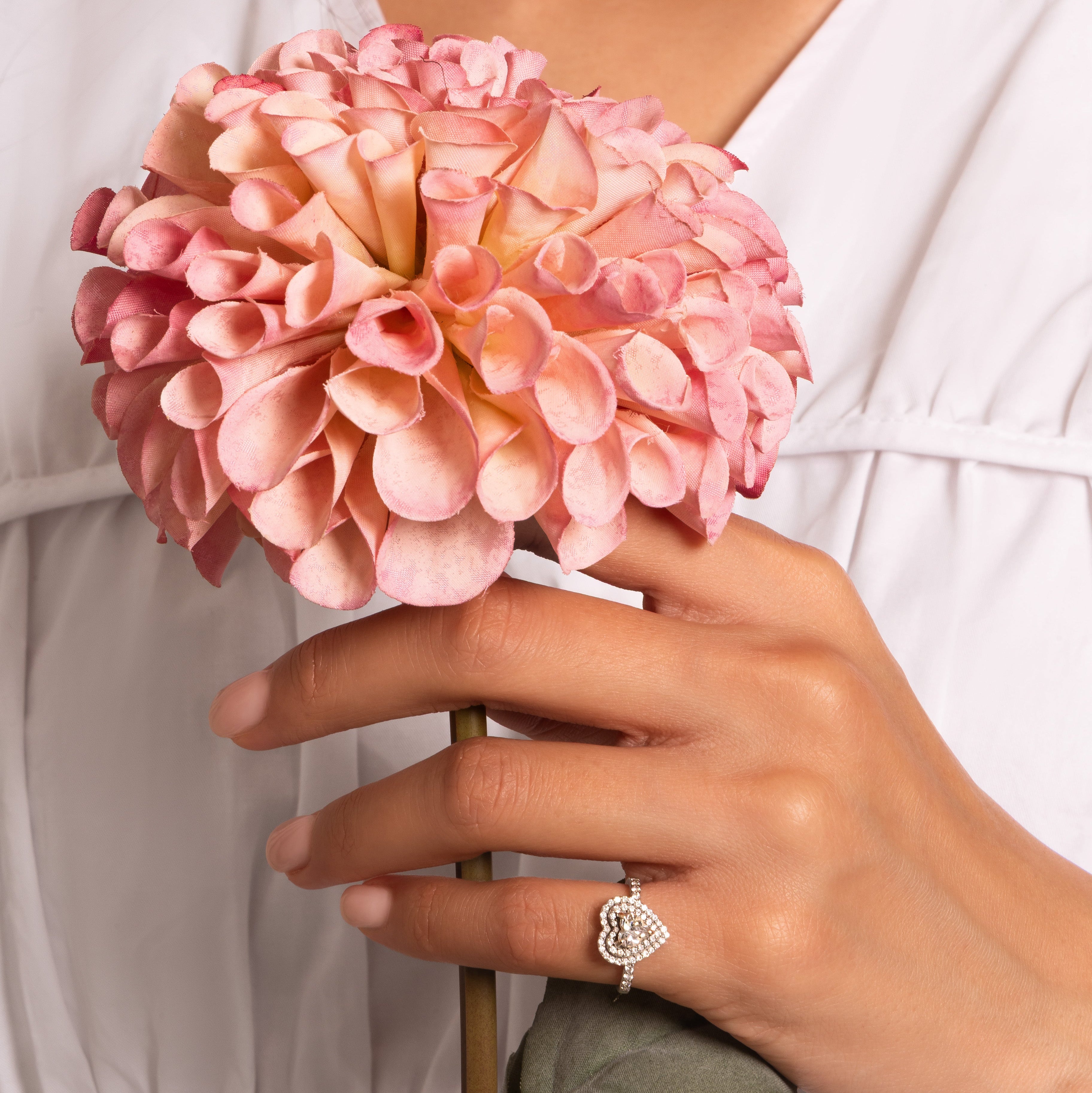 Hand holding a pink flower with a blurred white background